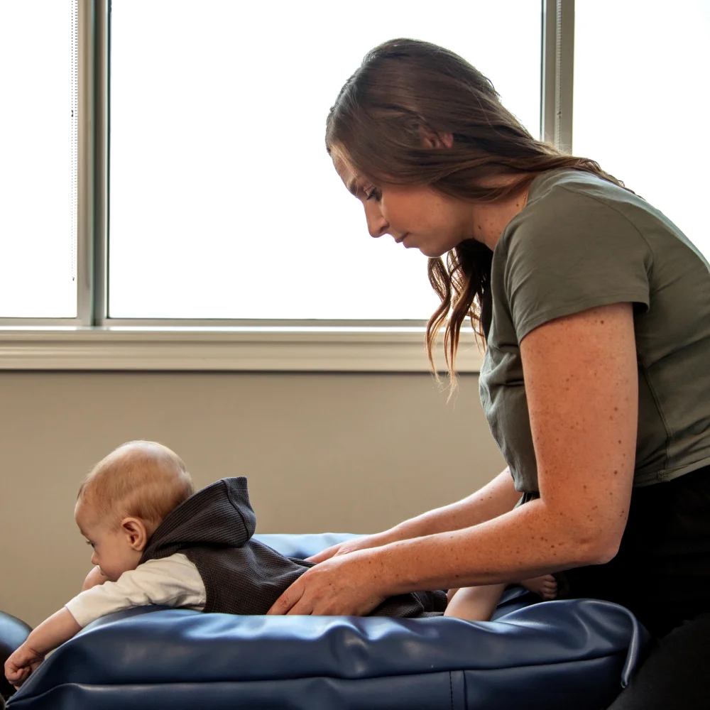 Female chiropractor performs adjustment on infant laying on chiropractic table